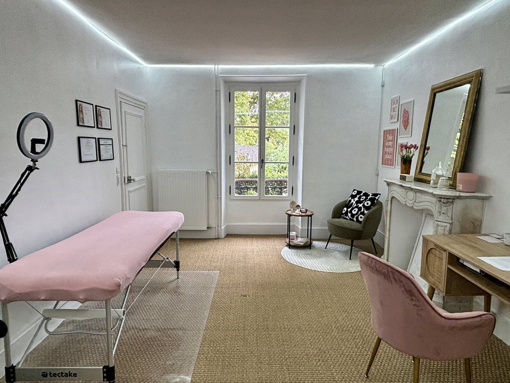 La pièce de l'institut : une fenêtre donnant sur le jardin, une table de soin, un miroir ancien, une cheminée en marbre et des tulipes roses.